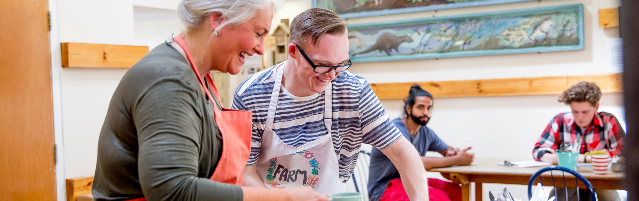 Two people wearing aprons and making food together in a cafe setting.