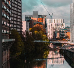 Street scene in Manchester. Tall buildings overlooking a tree lined river with a crane in the background.