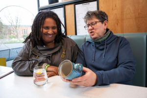 A photo of two people in a cafe. They are both admiring a handmade mug.