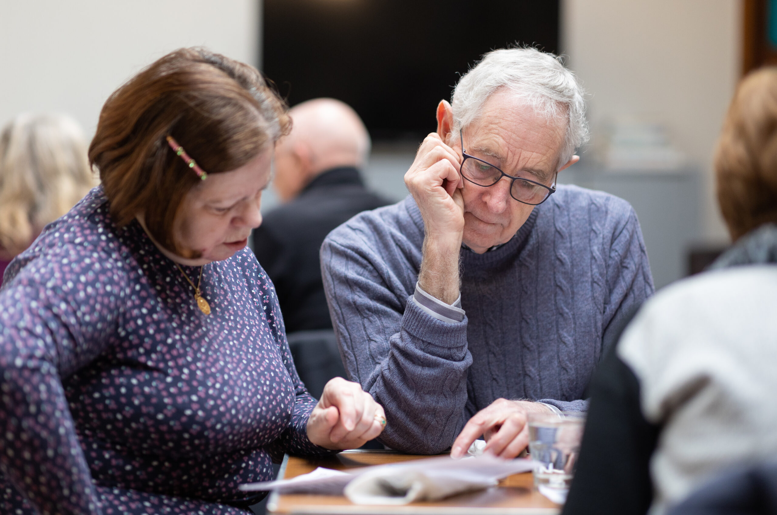 A photo of two people sat at a table reading a document