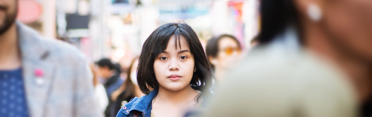 A close-up photo of a young woman walking through a busy crowd. The people around her are blurred.