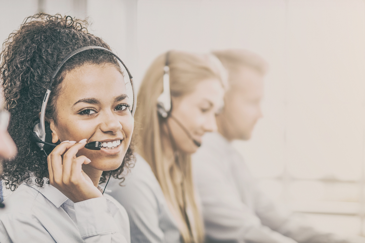 A photo of a few people taking calls with a headset. They are all sat at the same desk