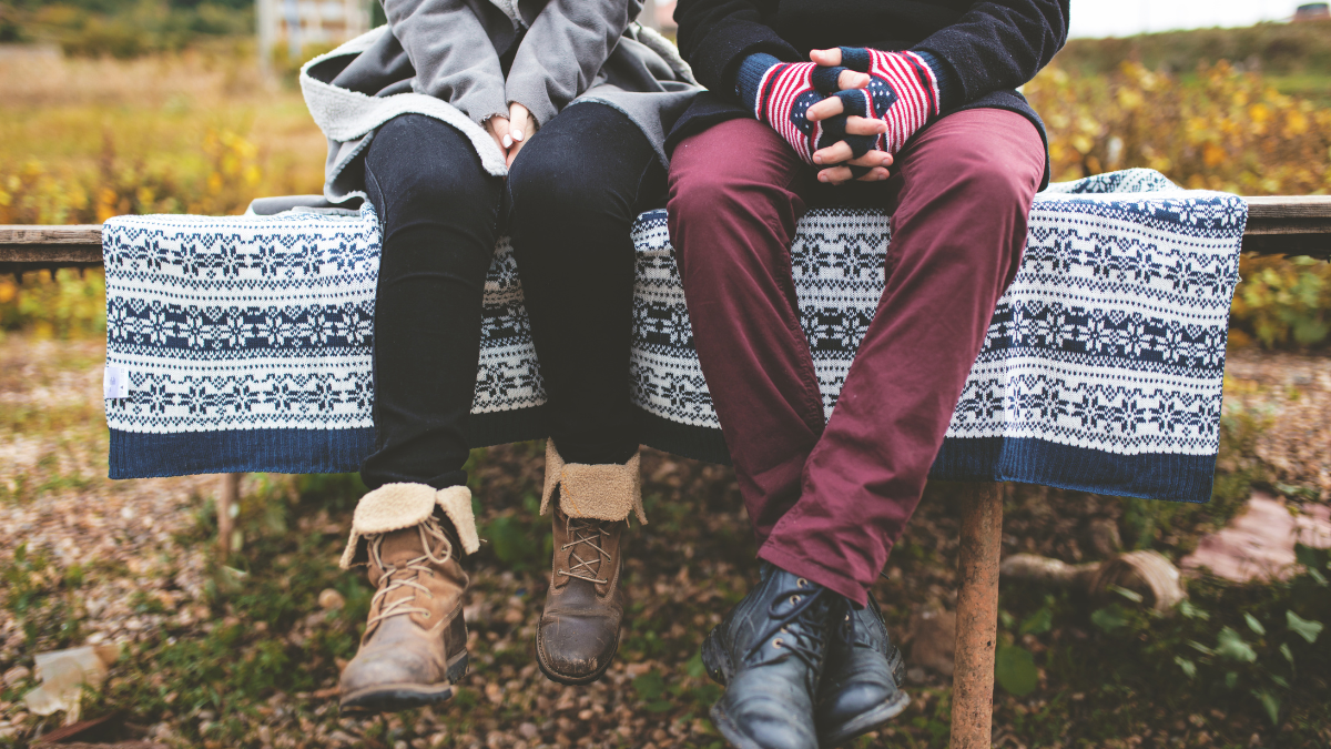 A photo of two people dangling their legs over a bench. They are wrapped up in winter clothes.