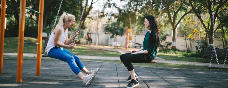 Two young people sit facing each other on a swing