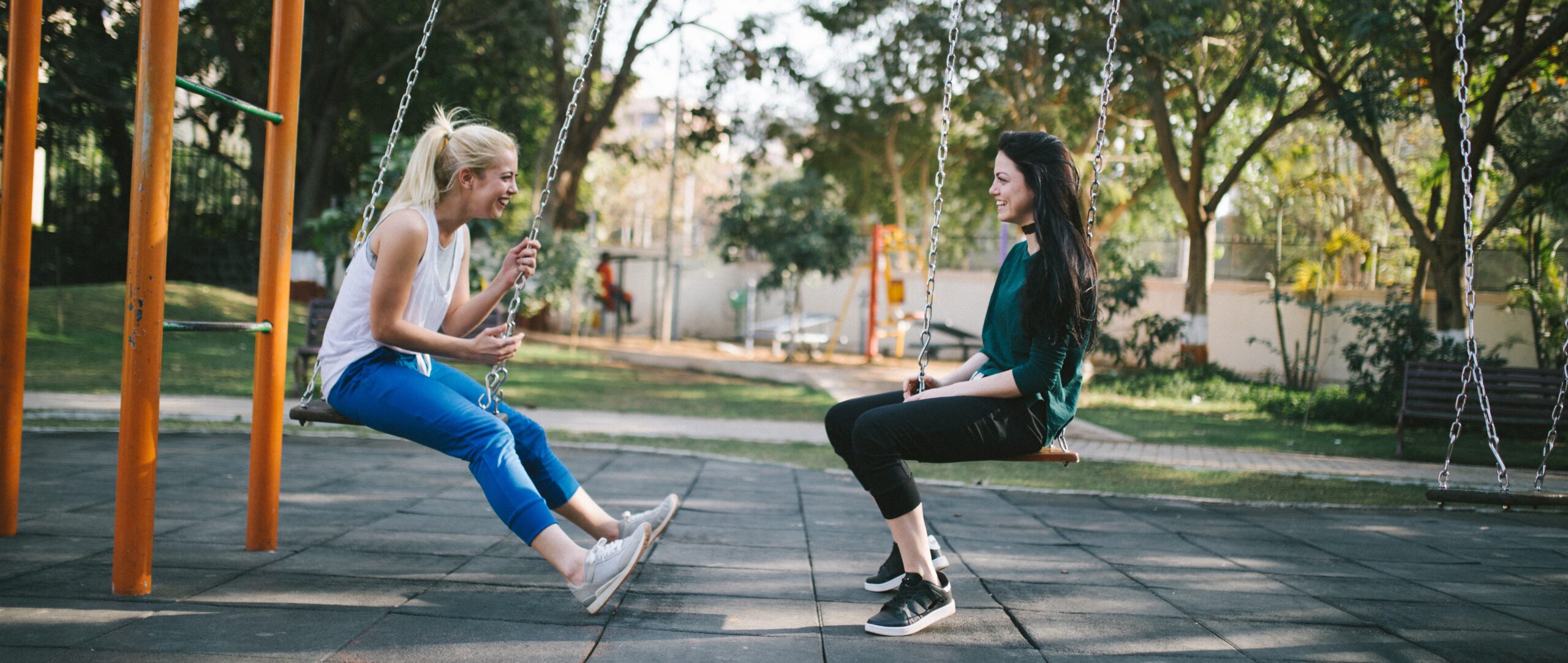 Two young people sit facing each other on a swing