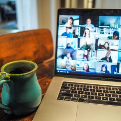 image of coffee cup on table next to laptop, screen filled with faces on an online meeting.