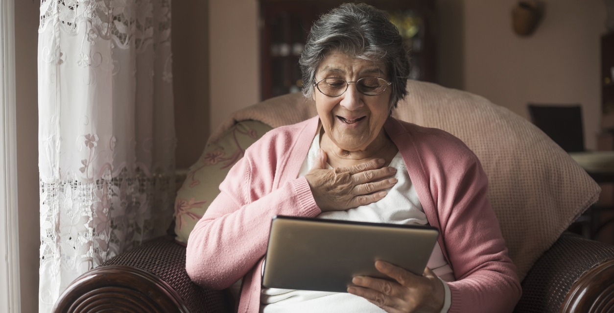 An older woman laughing as she uses a tablet