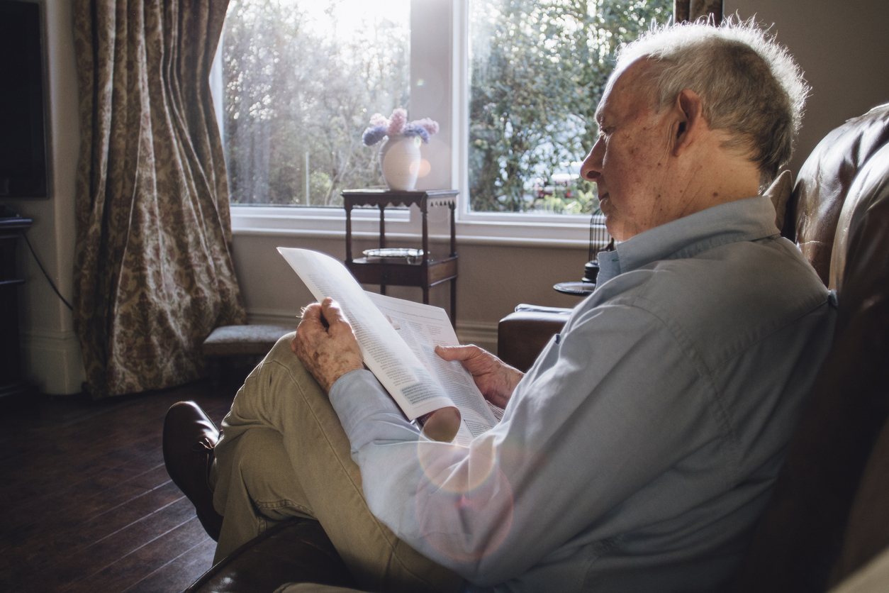 Senior man sitting alone in the living room of his home, reading a magazine.