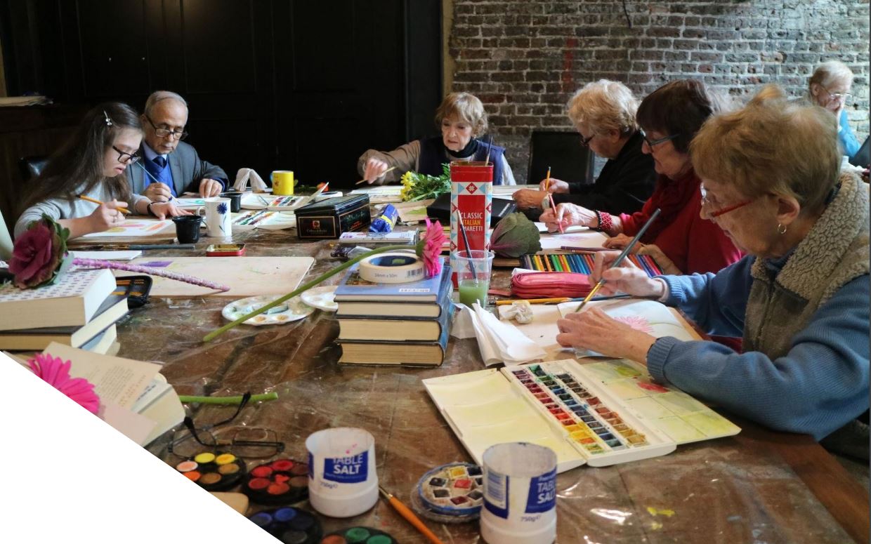 Group of older people sitting at a table painting and drawing together